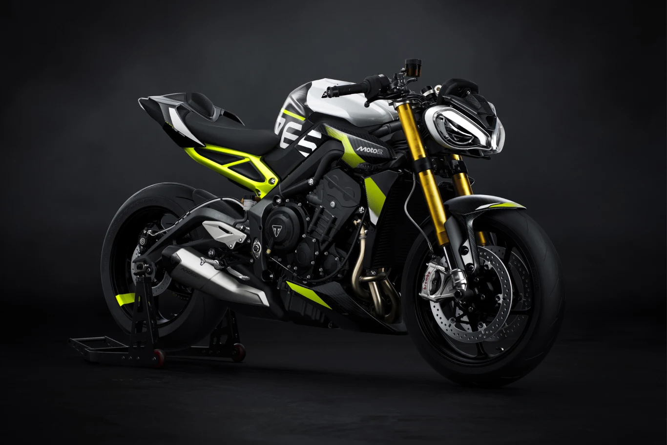 Wersji tego modelu nie da się pomylić - napis Moto2 zdradza wszystko. Sportowy motocykl Triumph Speed Triple RS z czarno-biało-żółtą kolorystyką na tle ciemnego studia, wyróżnia się nowoczesnym designem, agresywnymi liniami oraz widocznymi detalami technicznymi jak hamulce i zawieszenie.