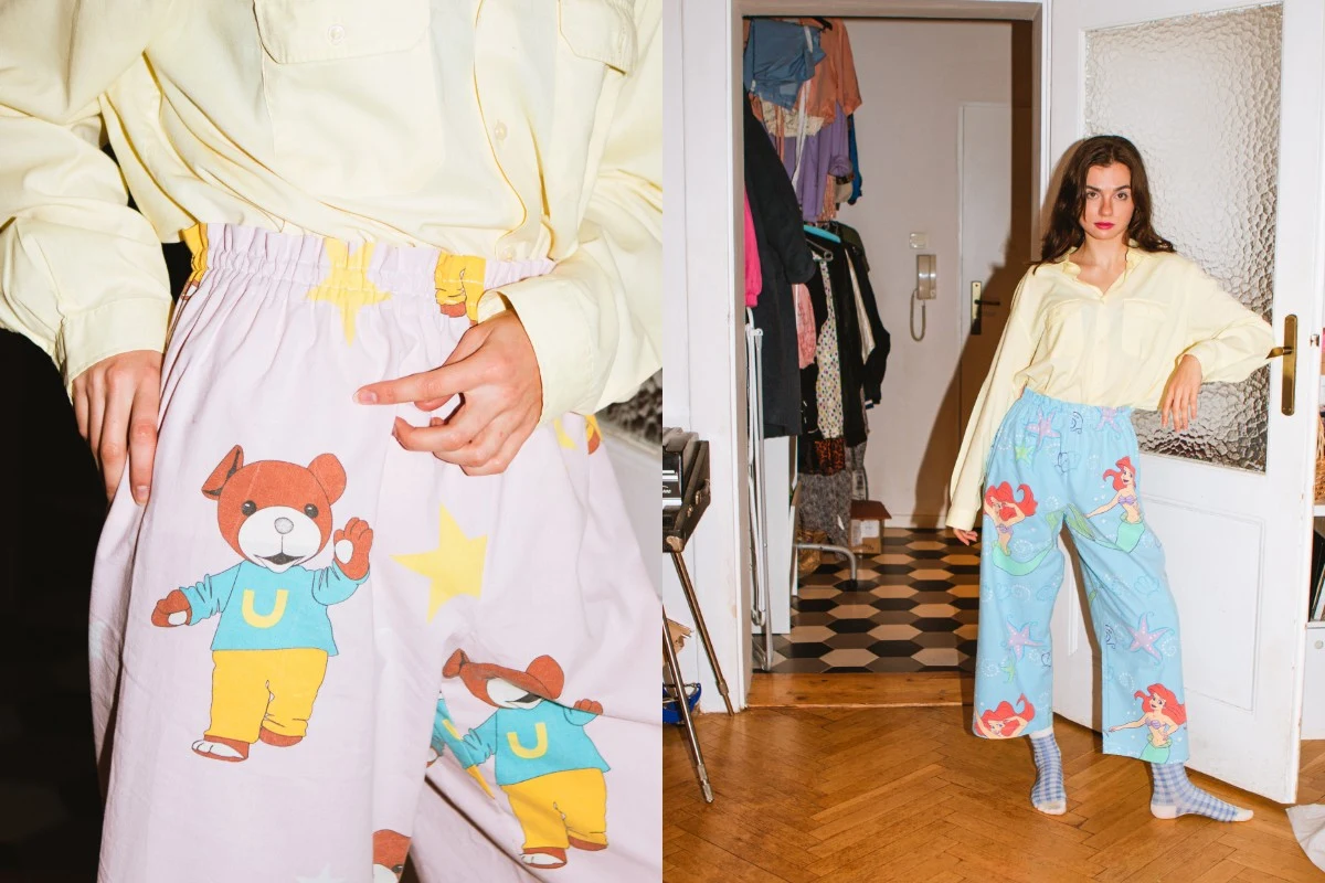 Młoda kobieta ubrana w luźną, żółtą koszulę i kolorowe spodnie z motywem misiów oraz gwiazdek stoi w mieszkaniu przy otwartych drzwiach, na tle domowego wnętrza z widoczną szafą z ubraniami.
