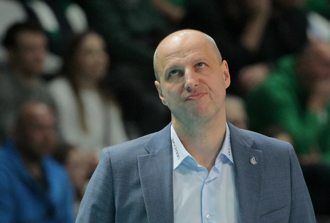 Łysy mężczyzna w garniturze z lekko zmartwioną lub rozczarowaną miną na twarzy, w tle rozmyta publiczność.