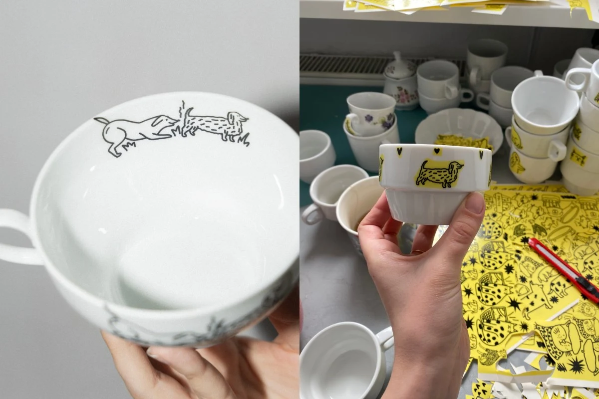 Porcelanowe kubki z czarno-żółtymi ilustracjami zwierząt wykonanymi w stylu rysunkowym. Jeden kubek trzymany jest w ręce, w tle widoczne liczne inne kubki oraz arkusze z wzorami.