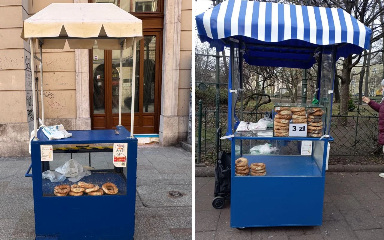 Dwa niebieskie stoiska z daszkami, ustawione na chodniku, prezentujące obwarzanki na sprzedaż. Jedno z nich posiada napis z ceną 3 złote, ciasteczka równomiernie ułożone w środku. W tle fragmenty elewacji i ogrodzenia miejskiego.
