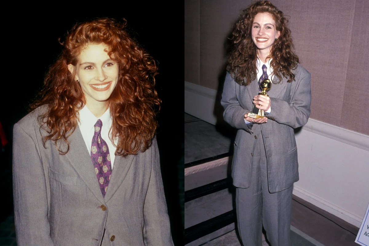 Młoda kobieta o długich, rudych włosach ubrana w szary, luźny garnitur i kolorowy krawat, szeroko uśmiechnięta, pozuje w jasnym pomieszczeniu oraz trzyma złotą statuetkę nagrody.