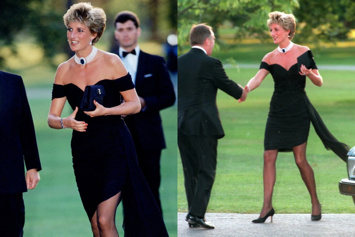 Elegancka kobieta w czarnej, wieczorowej sukience i naszyjniku, uśmiecha się i wita z mężczyzną na tle zielonego terenu, w otoczeniu osób w formalnych strojach.