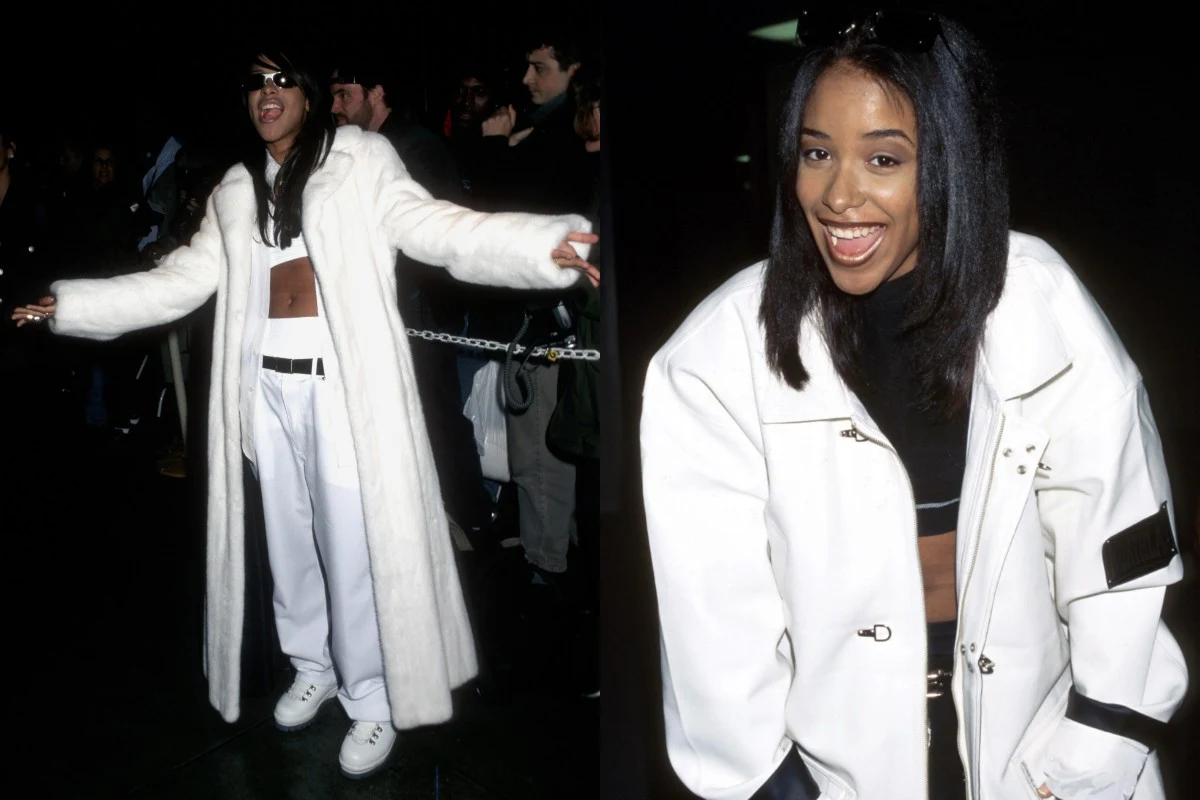 Młoda kobieta w białym długim płaszczu, białych spodniach i sportowych butach, odsłaniająca część brzucha, uśmiechnięta, z długimi prostymi włosami, pozuje w tłumie ludzi.