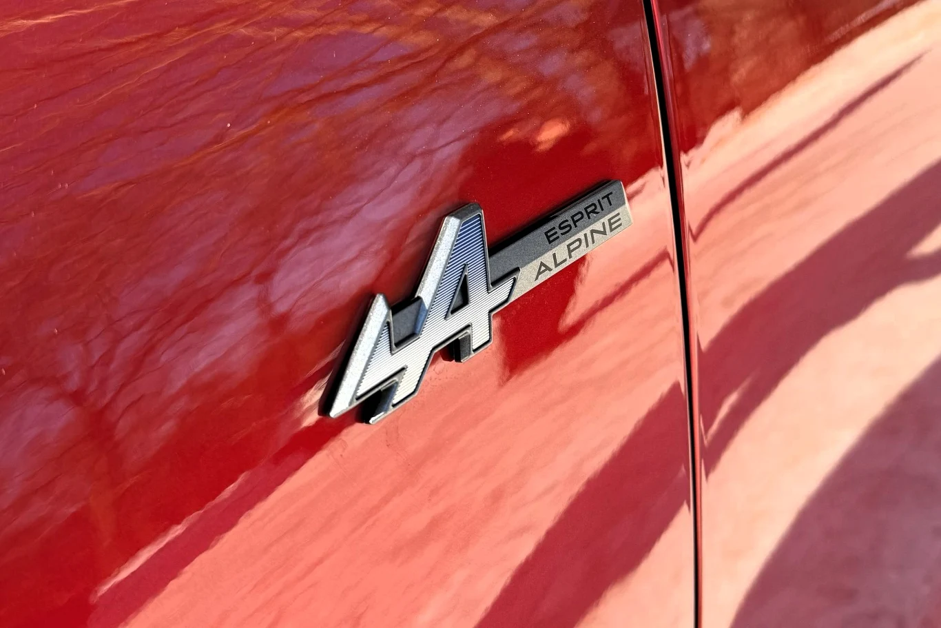 Czerwony lakierowany bok samochodu z widocznym chromowanym emblematem Alpine oraz napisem Esprit Alpine.