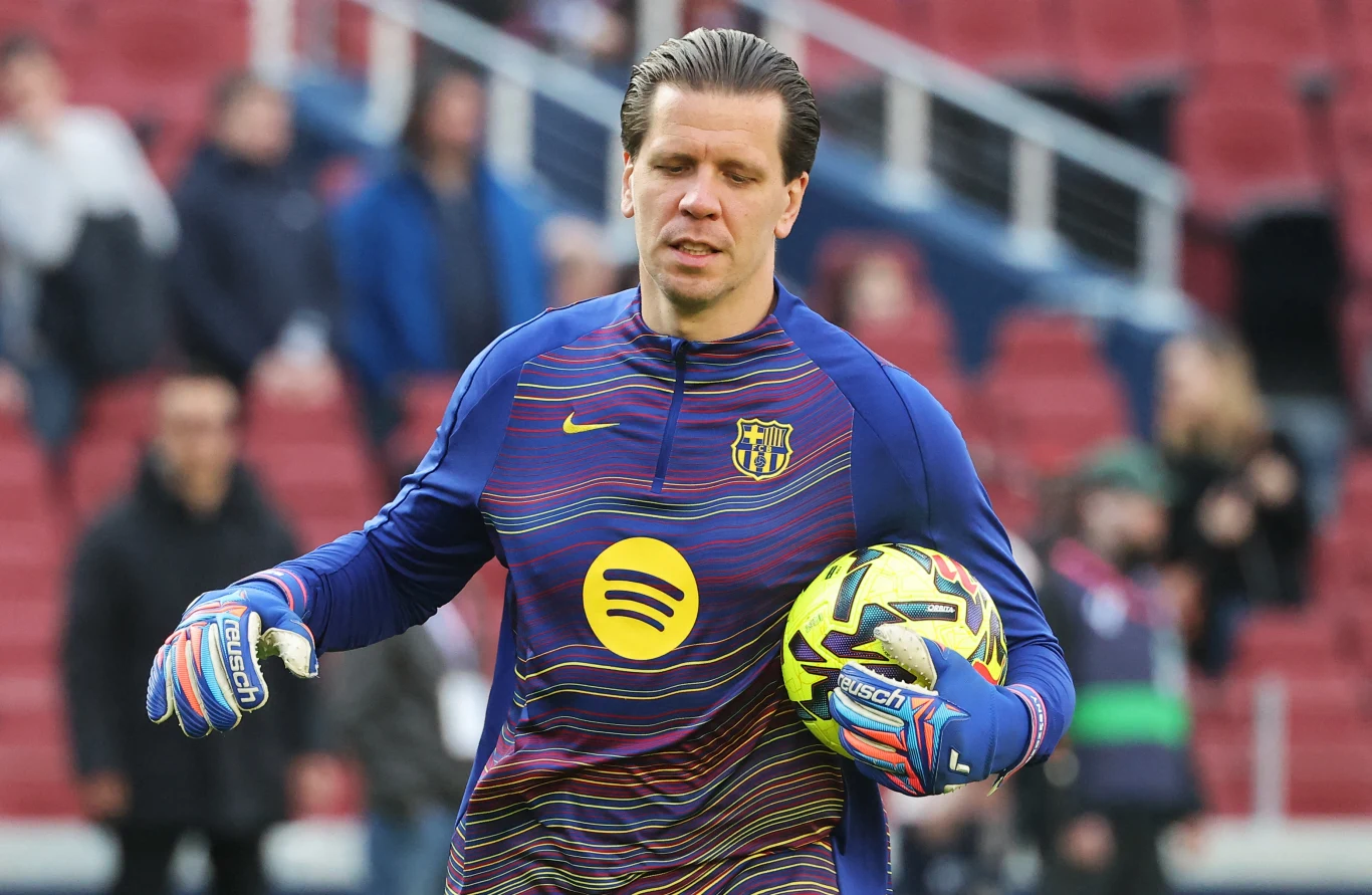 Wojciech Szczęsny Bramkarz w stroju treningowym FC Barcelona trzyma piłkę na stadionie, w tle widoczne rozmazane sylwetki ludzi i trybuny.