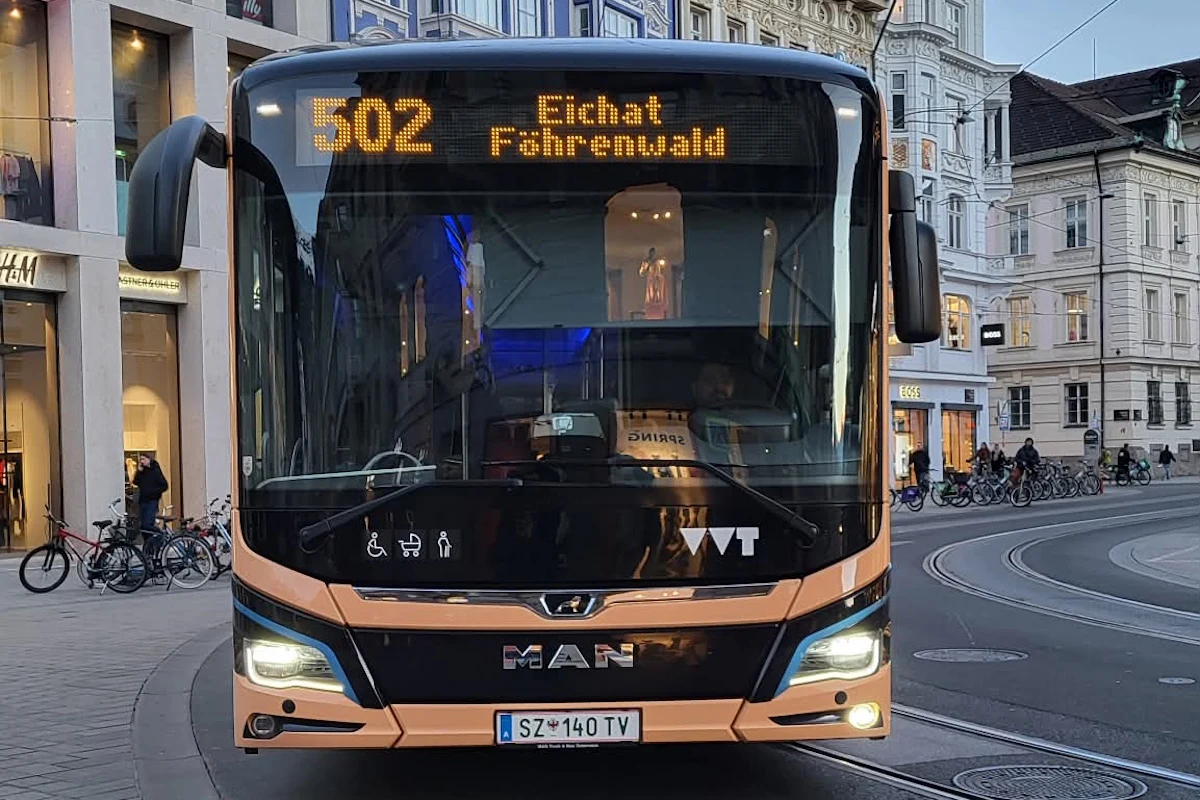 Autobus miejski marki MAN zatrzymany na przystanku w centrum miasta, na wyświetlaczu informacja o linii 502 do Eichat Fohrenwald, w tle zabudowa miejska z witrynami sklepów i zaparkowanymi rowerami.