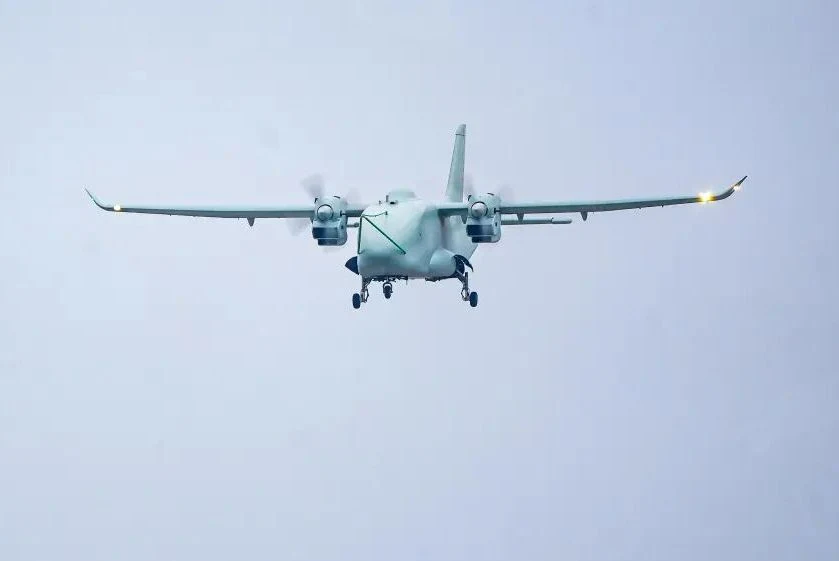 Dwusilnikowy samolot z rozświetlonymi światłami na skrzydłach leci na tle jasnego, pochmurnego nieba.