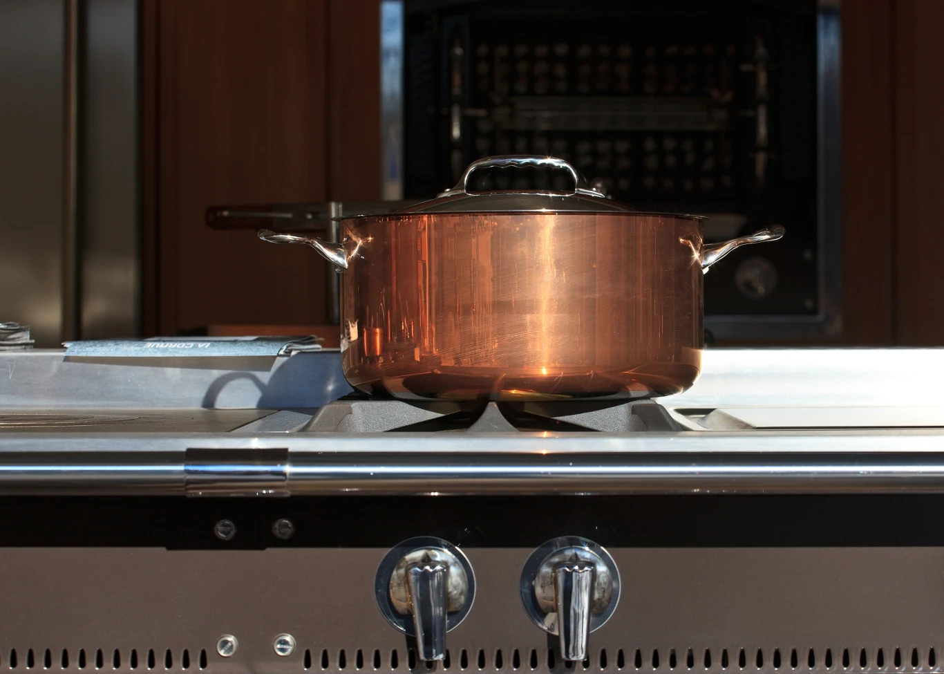 Zanim zdecydujesz się na zakup eleganckiego zestawu miedzianych garnków, miej pewność, że posiadają atesty Miedziany garnek z pokrywką stoi na kuchence gazowej, w tle widoczny piekarnik.