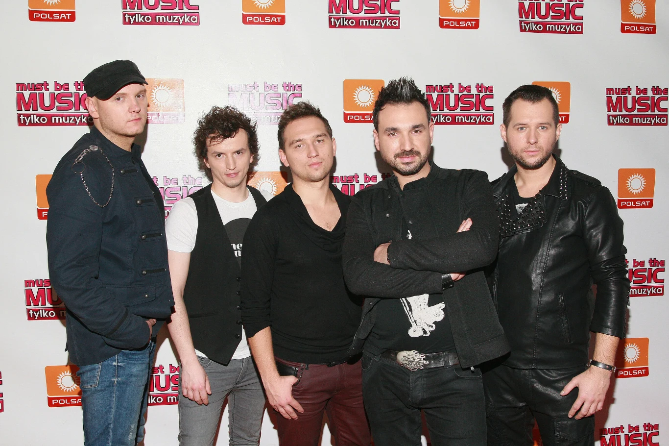 Grupa pięciu mężczyzn stoi razem na tle ścianki z logo programu Must Be The Music oraz telewizji Polsat, wszyscy ubrani są w casualowe stroje, część ma zarzucone ręce na siebie.