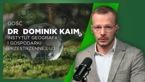 Mężczyzna w jasnej marynarce i białej koszuli siedzi przy mikrofonie, patrząc w stronę aparatu. W tle widoczny jest wizerunek szklanej kuli ziemskiej na tle zielonego mchu oraz napisy informujące o gościu, doktorze Dominiku Kaimie z Instytutu Geografii...