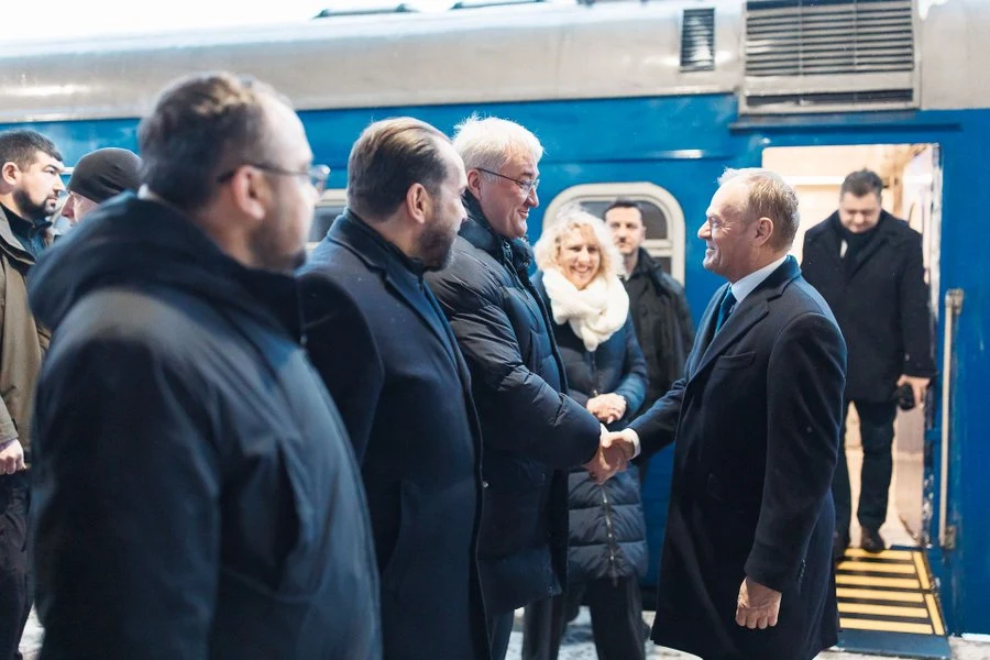 Donald Tusk z wizytą w Kijowie Grupa osób w eleganckich ubraniach wita się na peronie przy niebieskim pociągu, dwie osoby ściskają sobie dłonie, w tle widać ludzi uśmiechniętych i obserwujących sytuację.