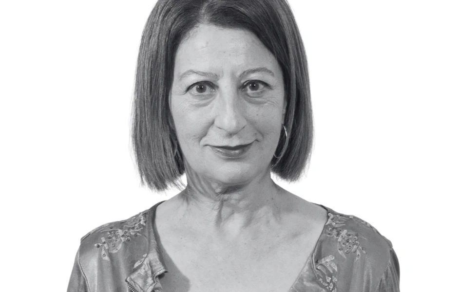 Kobieta o krótkich, prostych, ciemnych włosach, ubrana w elegancką bluzkę z delikatnym wzorem, patrząca prosto w obiektyw na białym tle.