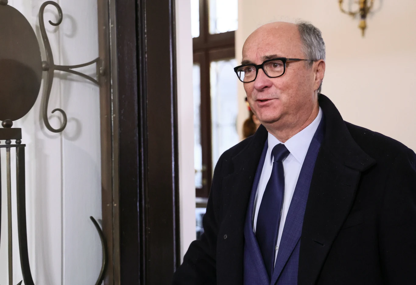 Zdaniem Jarosława Flisa krytyka ze strony USA nie zaszkodzi marszałkowi Czarzastemu Mężczyzna w okularach ubrany w garnitur i płaszcz, stojący we wnętrzu budynku przy otwartych drzwiach, w tle widoczna dekoracja ścienna i okno.