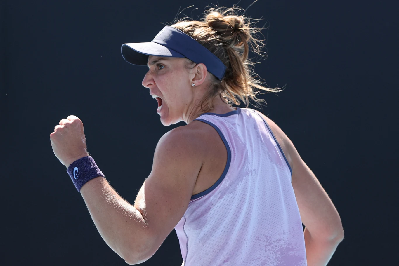 Beatriz Haddad Maia Tenisistka w sportowej koszulce i opasce na ręku wykonuje gest zwycięstwa, z wyrazem intensywnej emocji na twarzy, na tle ciemnego, neutralnego tła.