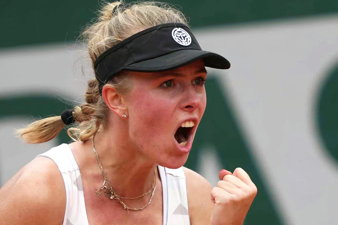 Zbliżenie na zawodniczkę tenisa w czarnej opasce, wyrażającą silne emocje po zwycięskiej akcji. Zaciśnięta pięść oraz szeroko otwarte usta akcentują determinację i sportową pasję.