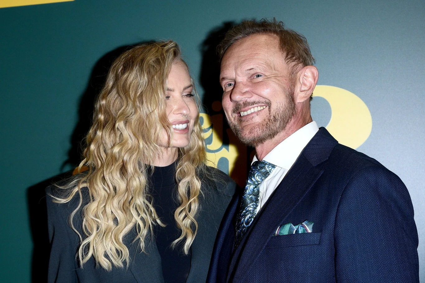 Fotoreporterzy nie mogli oderwać oczu od Pazurów. Edyta wyglądała zjawiskowo Dwoje elegancko ubranych ludzi, kobieta z długimi falowanymi blond włosami ubrana na czarno i mężczyzna w granatowej marynarce z białą koszulą oraz wzorzystym krawatem, stoją obok siebie i uśmiechają się szeroko. Tło stanowi zielony panel z żółtym napi...