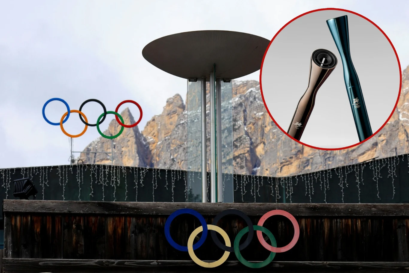 Stadion olimpijski ze stojącym zniczem oraz olimpijskie koła na tle gór. W prawym górnym rogu kadr ze zdjęciem pochodni olimpijskiej.