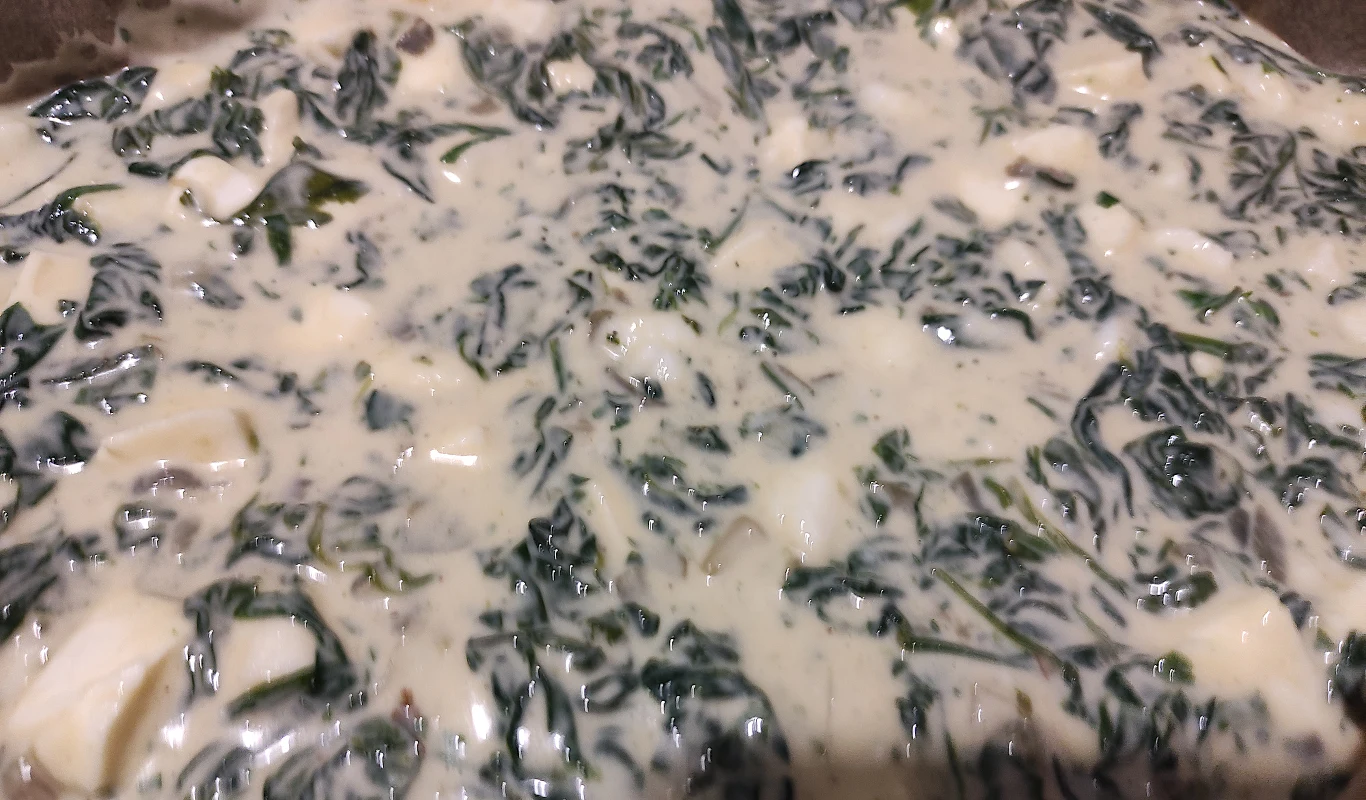 Ciasto wymieszaj ze szpinakiem, mozzarellą i pietruszką Masa z liści szpinaku zatopionych w jasnym, kremowym sosie, z wyraźnie widocznymi kawałkami białego sera.