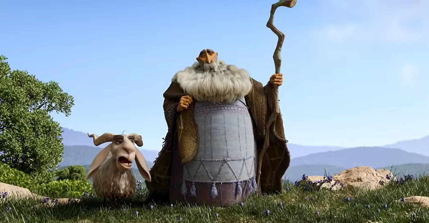 Kadr z filmu "David" Stary czarodziej z siwą brodą i szatą stoi na łące, trzymając zakrzywioną laskę w prawej ręce, obok niego śmiesznie wyglądająca koza z wytrzeszczonymi oczami. W tle pagórkowaty krajobraz i błękitne niebo.