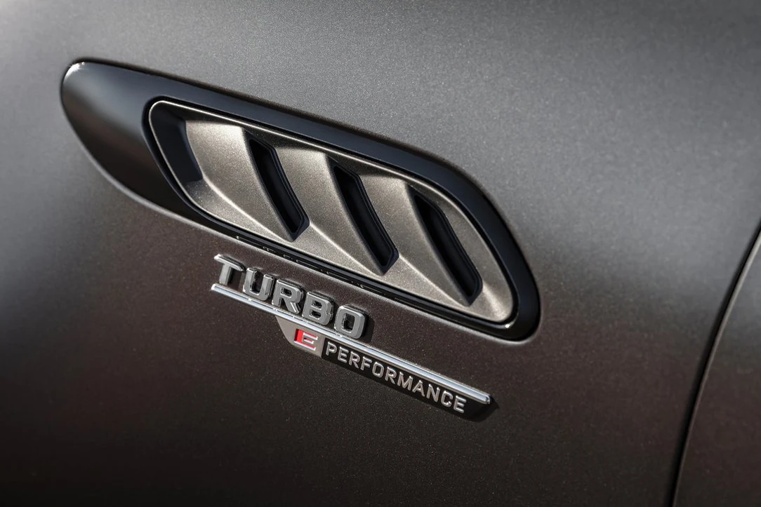 Logo Turbo Performance obok chromowanej kratki wentylacyjnej na lakierowanej, szarej karoserii samochodu.