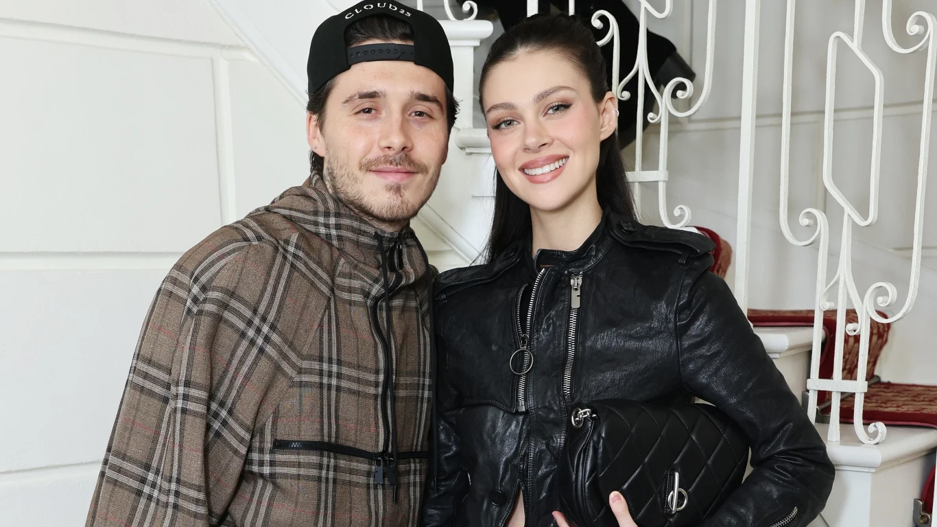 Brooklyn Beckham i Nicola Peltz Młody mężczyzna w czapce z daszkiem i kurtce w kratę stoi obok uśmiechniętej kobiety w czarnej skórzanej kurtce i z torebką, oboje pozują razem na tle białych schodów.