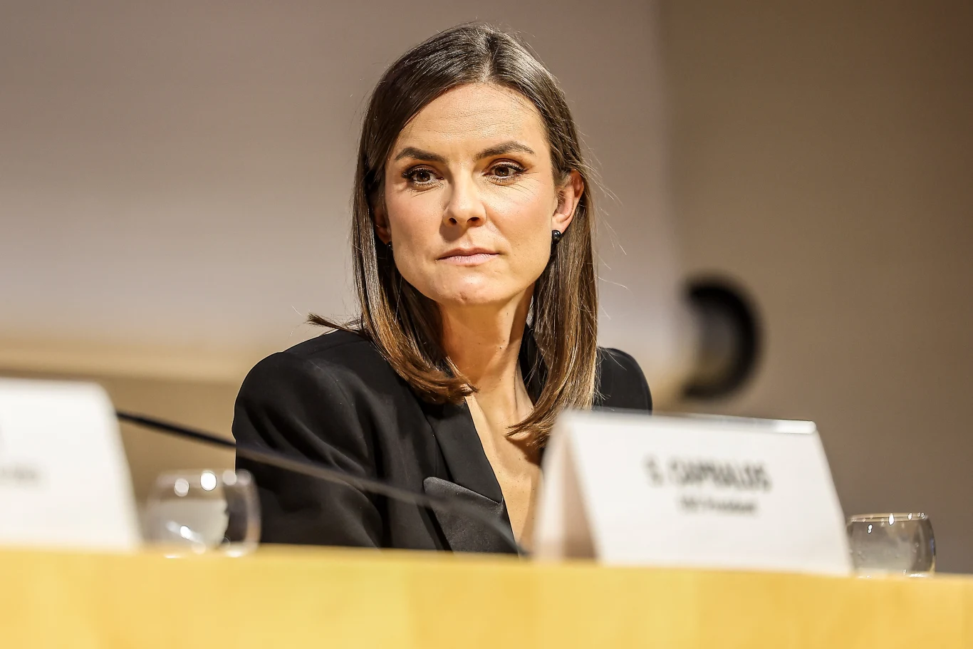 Maja Włoszczowska Kobieta o średnich brązowych włosach w formalnym stroju siedzi przy stole konferencyjnym, przed nią stoi tabliczka z nazwiskiem oraz dwa kieliszki do wody.