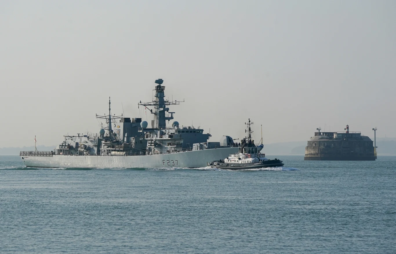 Fregata typu 23 HMS Richmond należąca do Królewskiej Marynarki Wojennej Okręt wojenny eskortowany przez holownik płynie po spokojnej wodzie, w tle widoczna jest forteca znajdująca się na niewielkiej wyspie.