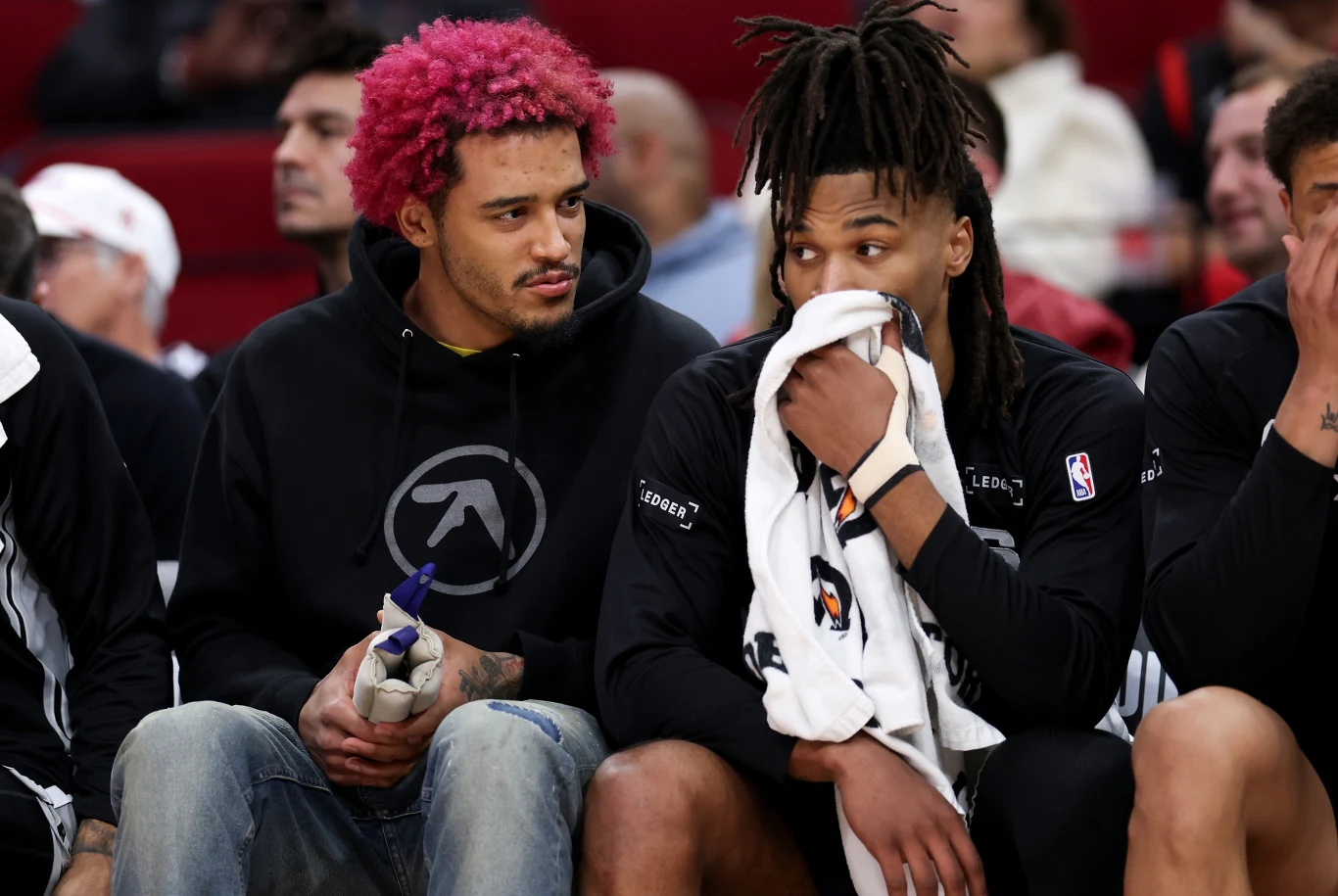 Jeremy Sochan i Stephon Castle Dwóch młodych mężczyzn siedzących na ławce podczas meczu koszykówki, jeden z różowymi włosami w czarnej bluzie, drugi z dredami, trzymający ręcznik przy twarzy. W tle widoczne inne osoby.