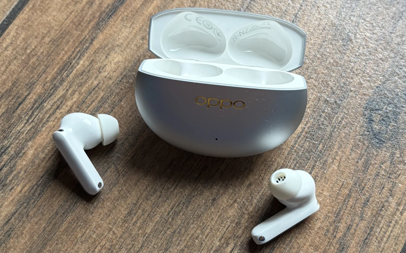 Słuchawki bezprzewodowe OPPO Enco X3s. Białe bezprzewodowe słuchawki douszne wraz z otwartym etui ładującym marki Oppo leżące na drewnianej powierzchni.