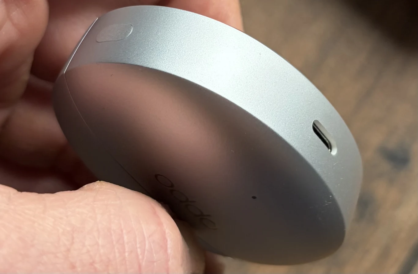 Pudełeczko ładujące OPPO Enco X3s. Okrągłe, srebrne urządzenie elektroniczne trzymane w dłoni, z widocznym portem USB typu C na jednym z boków.