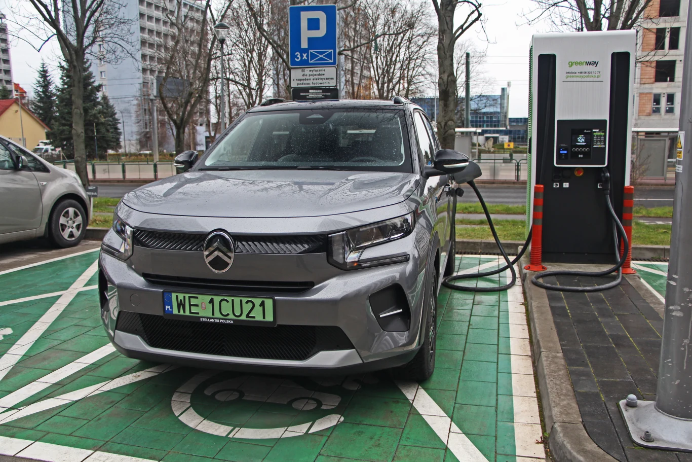 Stellantis mocno zainwestował w rozwój samochodów elektrycznych, również tych tanich. Teraz zmuszony jest zrewidować swoje plany, co wiąże się z ogromnymi kosztami Szary samochód elektryczny marki Citroën podczas ładowania przy stacji ładowania GreenWay, stojący na miejscu parkingowym przeznaczonym wyłącznie dla pojazdów elektrycznych, w otoczeniu budynków mieszkalnych.