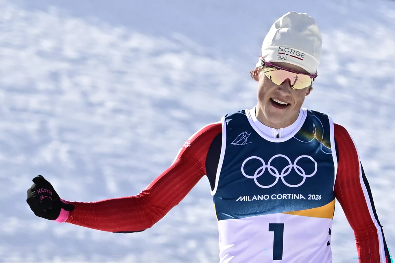 Johannes Hoesflot Klaebo, norweski triumfator biegu łączonego 10+10 km Narciarz biegający w stroju reprezentacji Norwegii, w sportowej czapce i okularach przeciwsłonecznych, bierze udział w zimowych igrzyskach olimpijskich Milano Cortina 2026, dynamiczne ujęcie na tle śnieżnego krajobrazu.