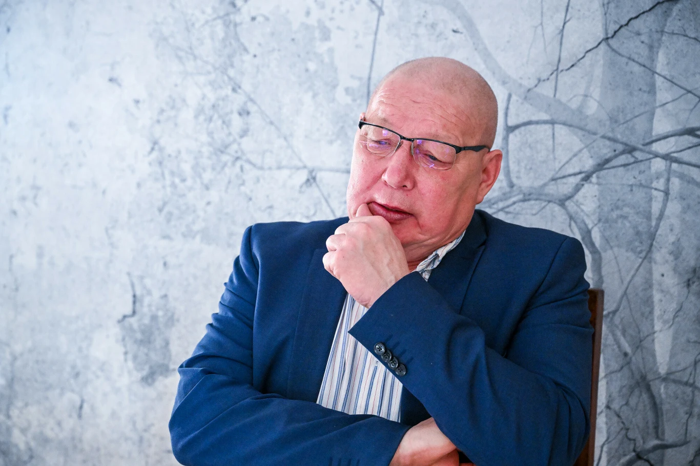 Krzysztof Jackowski przepowiada także pogodę Starszy mężczyzna w okularach ubrany w granatową marynarkę i koszulę, opiera głowę na dłoni, sprawia wrażenie zamyślonego, tło w odcieniach szarości z abstrakcyjnym wzorem.