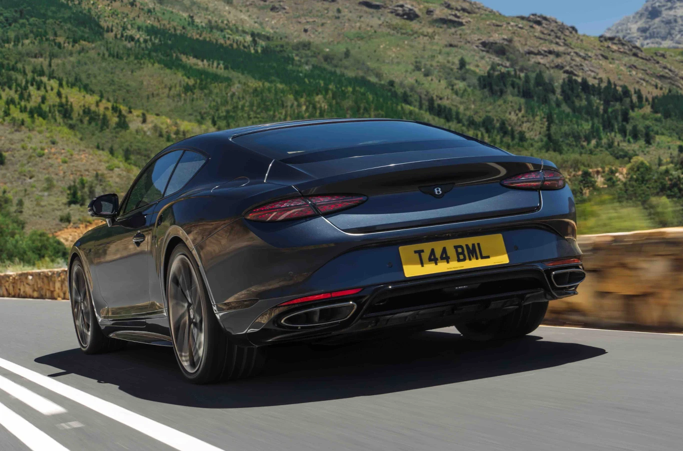 Nowy Continental S przyspiesza od 0 do 100 km/h w 3,5 s. Czarny luksusowy samochód sportowy jedzie asfaltową drogą przez górski krajobraz, w tle widać roślinność i skaliste wzgórza.