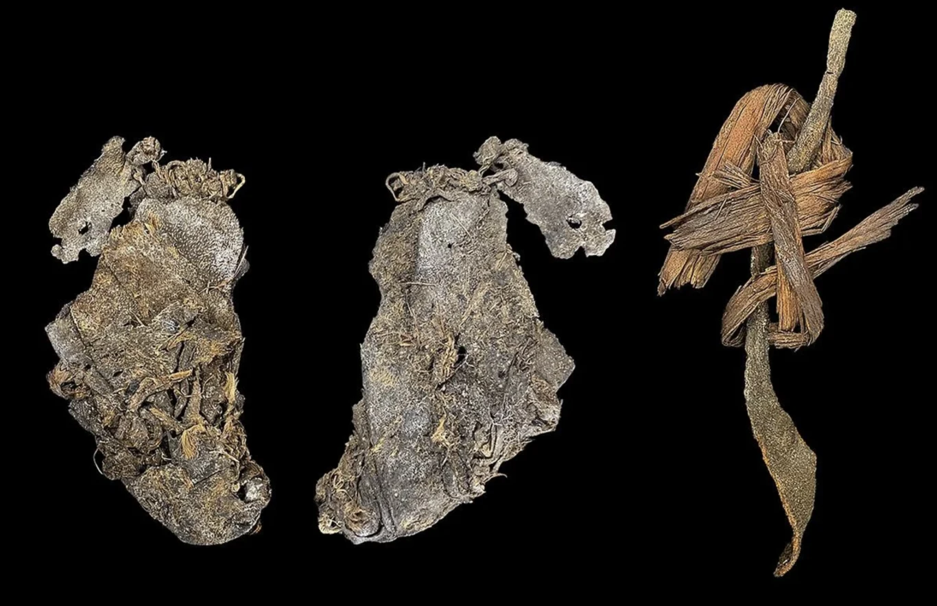 Najstarsza zszyta skóra odkryta w jaskini w Oregonie sugeruje istnienie wczesnych ubrań Dwie stare, mocno zniszczone skórzane buty prezentowane obok siebie, po prawej stronie fragment skórzanego paska, wszystko na czarnym tle podkreślającym szczegóły strukturalne tych przedmiotów.