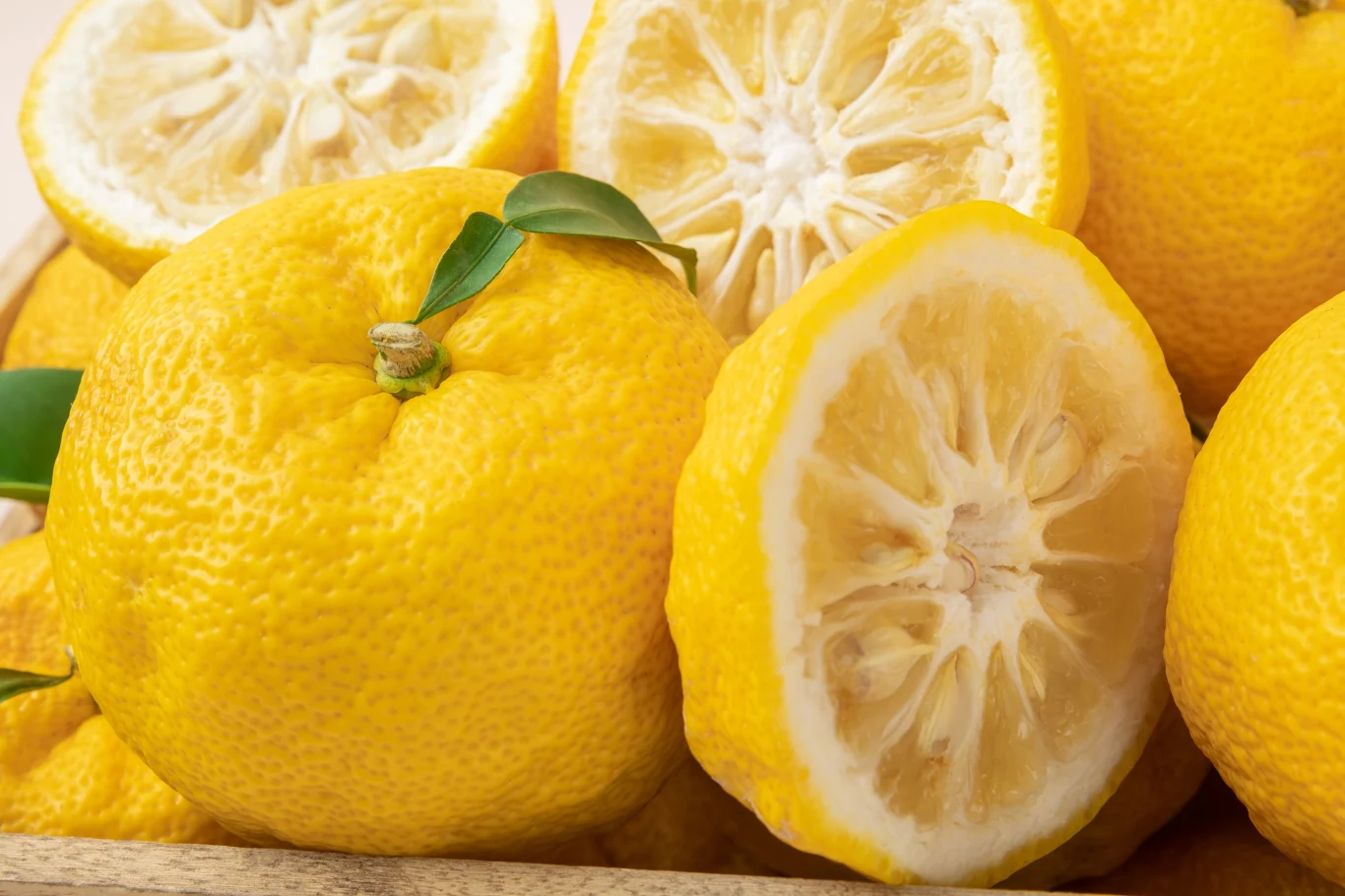 Przypomina cytrynę, choć kształtem bardziej mandarynkę. Ten egzotyczny owoc ma trzykrotnie więcej witaminy C Dojrzałe, żółte owoce cytrusowe, kilka przekrojonych na pół, z wyraźnie widocznym miąższem oraz liśćmi, ułożone blisko siebie.