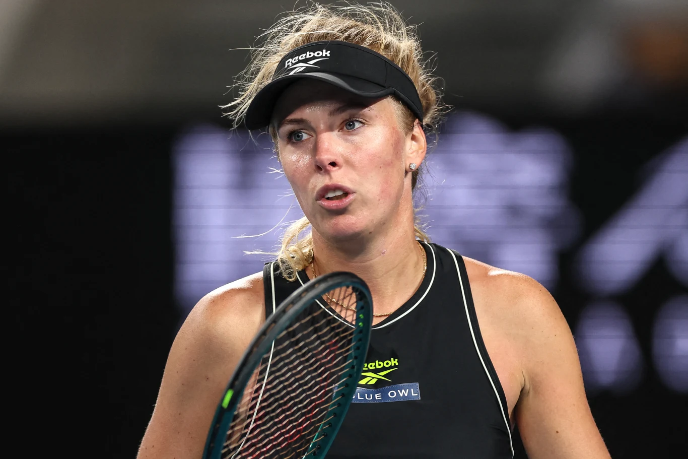 Magdalena Fręch Zawodniczka tenisa ubrana w sportową odzież z opaską Reebok i czarnym podkoszulkiem, trzymająca rakietę podczas meczu na kortach tenisowych, wyraz twarzy sugeruje skupienie i zmęczenie.