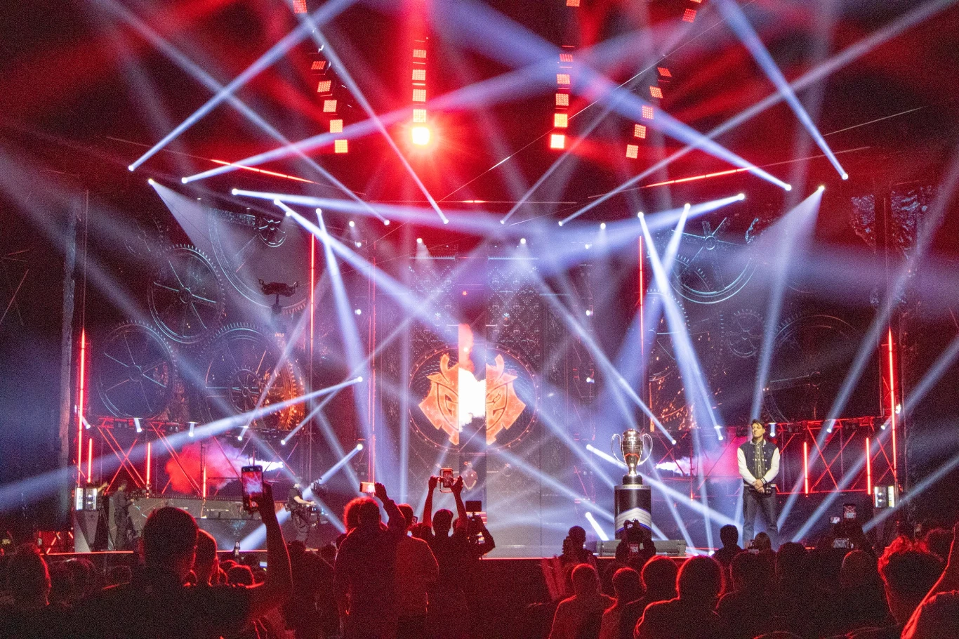 Kolorowa scena oświetlona jasnymi reflektorami, liczna publiczność skierowana w stronę centralnej części z dużym trofeum, wyraźna atmosfera uroczystości lub gali wręczenia nagród.