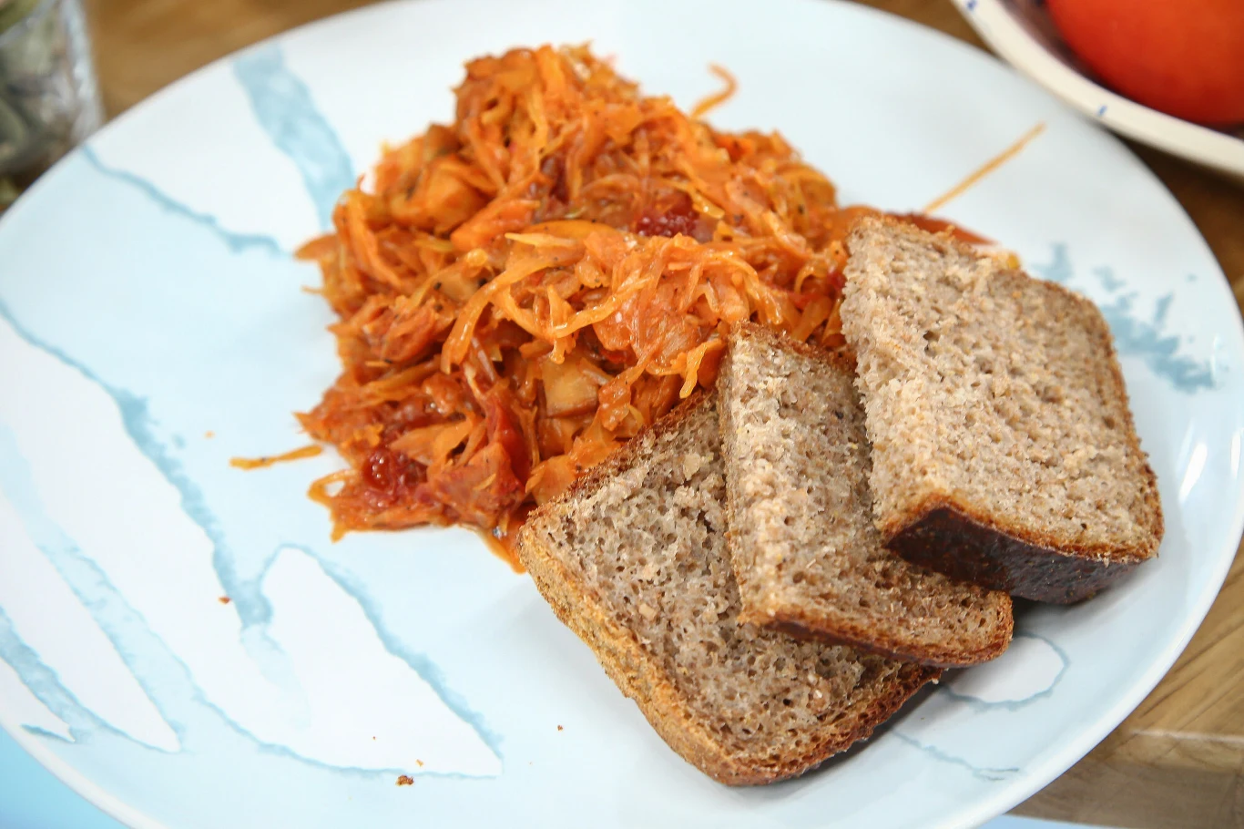 Jeśli w bigosie chcemy mieć pomidorowy dodatek, pamiętajmy by wybierać koncentrat, a nie ketchup Porcja duszonej kapusty z dodatkiem pomidorów i warzyw podana z trzema kromkami chleba razowego na jasnym talerzu.