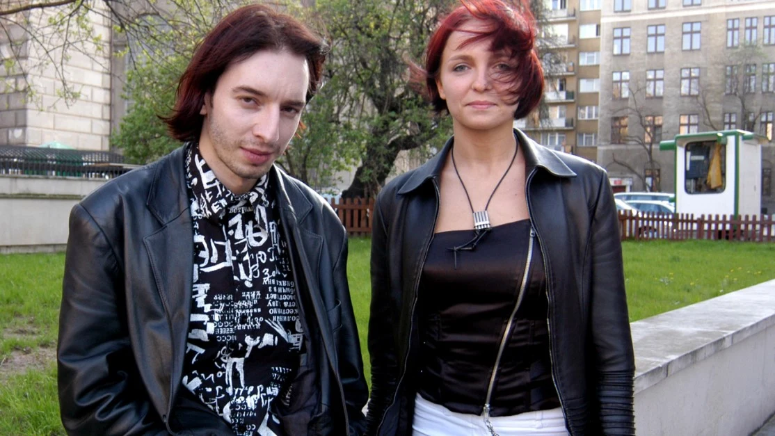 Adam Konkol, Anna Wyszkoni Dwoje młodych ludzi stoi na tle miejskiego skweru, kobieta ma krótkoczerwone włosy i czarną, skórzaną kurtkę, mężczyzna ma średniej długości włosy i wzorzysty t-shirt, oboje patrzą w stronę aparatu.