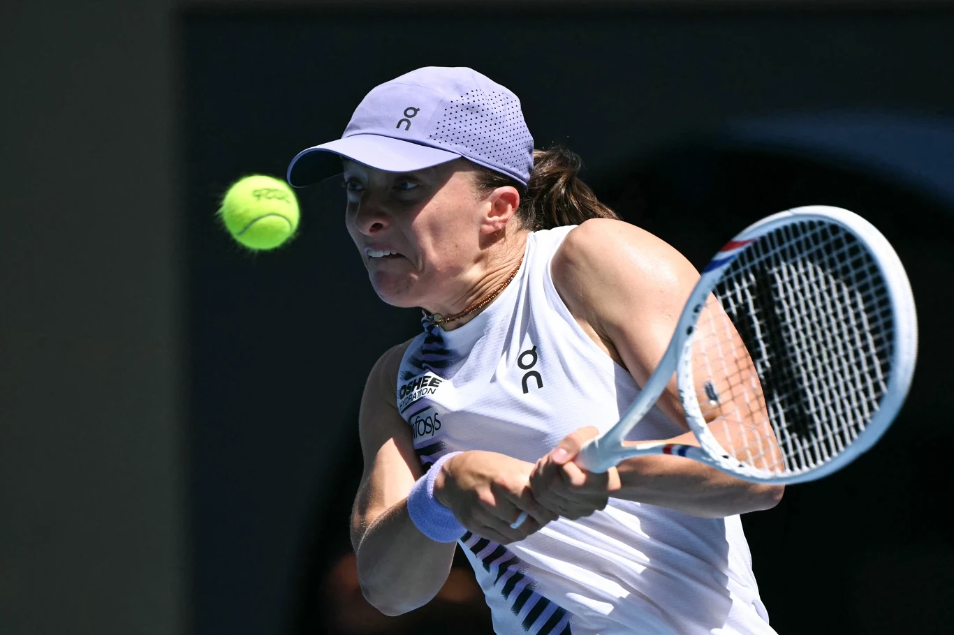 Iga Świątek rywalizowała o awans do trzeciej rundy WTA 1000 w Dosze Zawodniczka w sportowej czapce i białym stroju tenisowym skupiona na odbiciu nadlatującej piłki tenisowej rakietą podczas meczu na otwartym korcie.