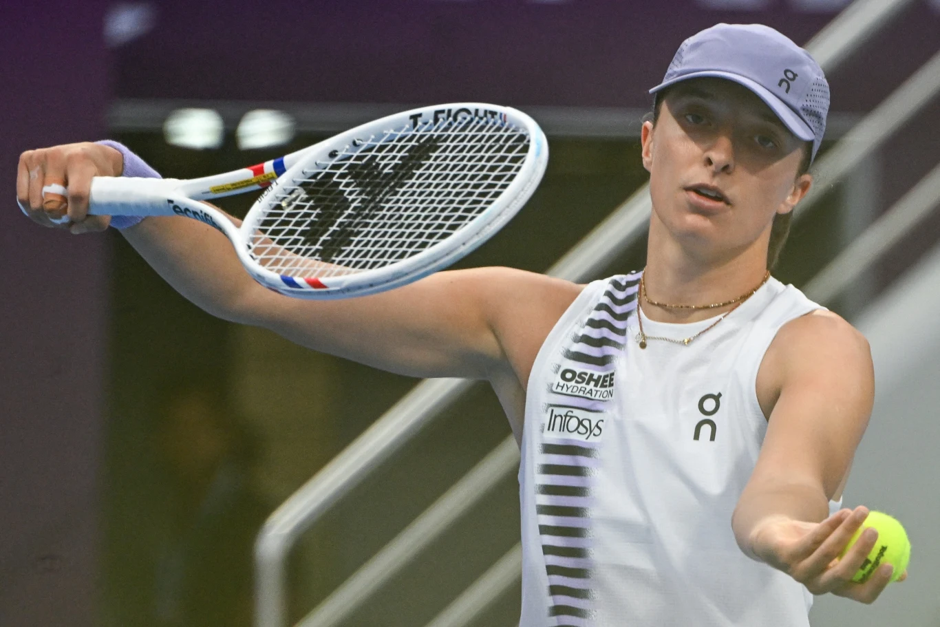 Iga Świątek Tenisistka w sportowym stroju serwuje podczas meczu, trzymając rakietę i piłkę tenisową na korcie o zdecydowanym wyrazie twarzy.