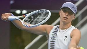 Tenisistka w sportowym stroju serwuje podczas meczu, trzymając rakietę i piłkę tenisową na korcie o zdecydowanym wyrazie twarzy.