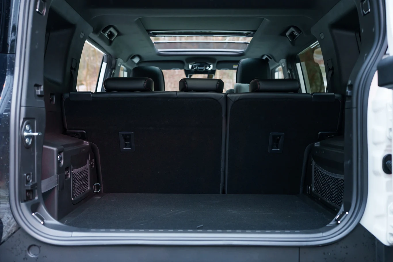 Bagażnik przestronnego samochodu terenowego z widocznymi siedzeniami w drugim rzędzie, czarne wnętrze, dużo miejsca na bagaże.