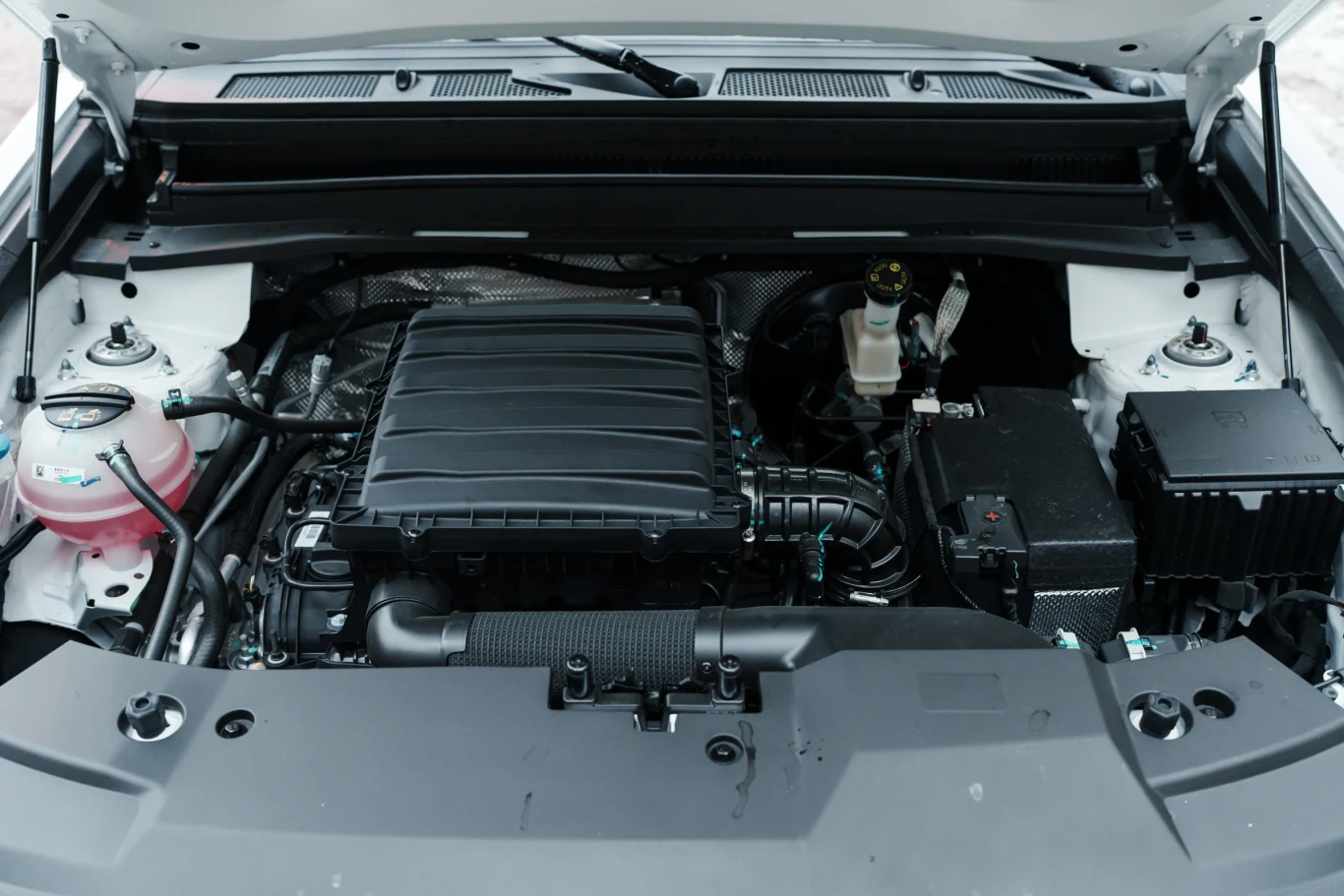 Silnik samochodowy z otwartą maską, widoczne elementy układu mechanicznego oraz instalacji elektrycznej, zbiornik płynu chłodniczego po lewej stronie oraz zbiornik płynu hamulcowego po prawej.