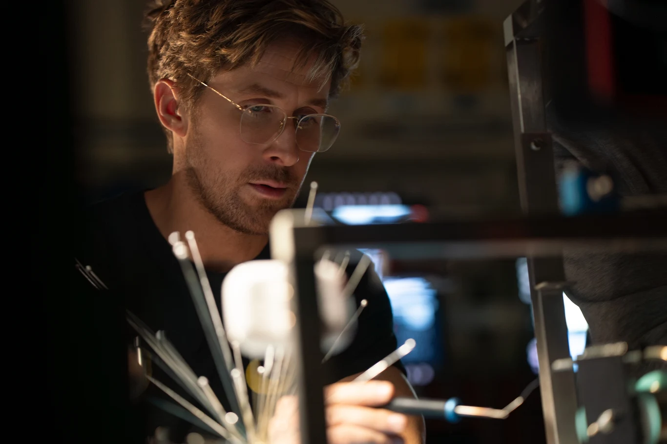 Ryan Gosling i "Projekt Hail Mary" Mężczyzna w okularach skupiony na pracy nad urządzeniem technicznym w laboratorium, otoczony metalowymi prętami i przyrządami badawczymi.