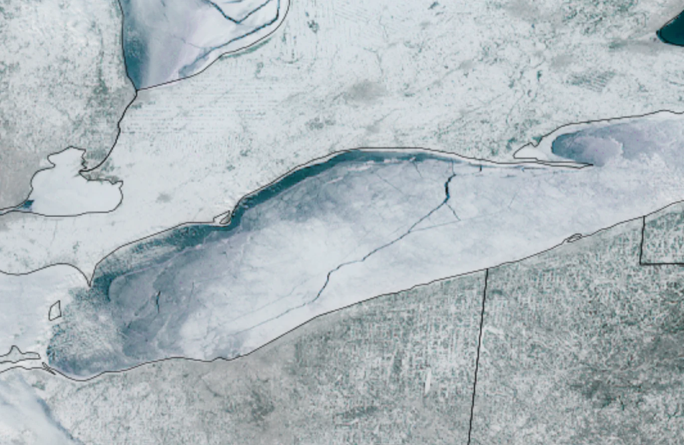 Na zamarzniętym jeziorze Erie pojawiła się 128-kilometrowa szczelina. Zamarznięte jezioro otoczone pokrywą śniegu z widocznymi pęknięciami lodu oraz zarysami linii brzegowej, całość ukazana w chłodnej, zimowej tonacji.