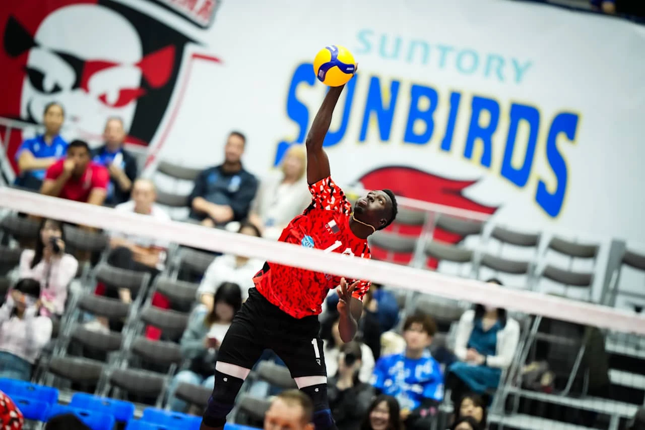 Noumory Keita Siatkarz w czerwonej koszulce uderza piłkę podczas meczu siatkówki halowej, w tle widoczna publiczność oraz duże logo zespołu Sunbirds na ścianie.