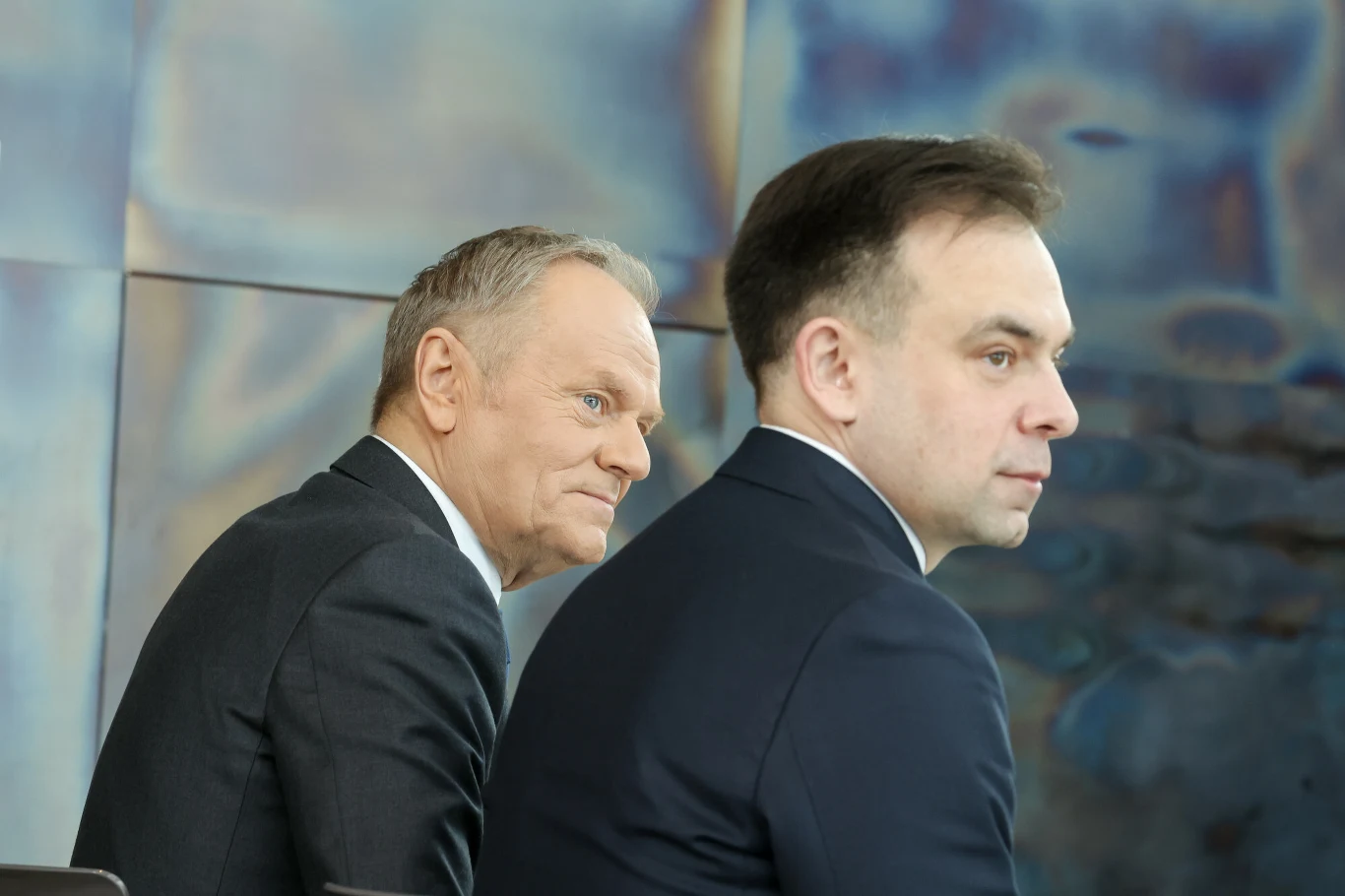 Premier Donald Tusk i minister finansów i gospodarki Andrzej Domański Dwóch mężczyzn w garniturach siedzi obok siebie, obaj są w średnim wieku, skupieni, tło rozmyte w chłodnych tonacjach.